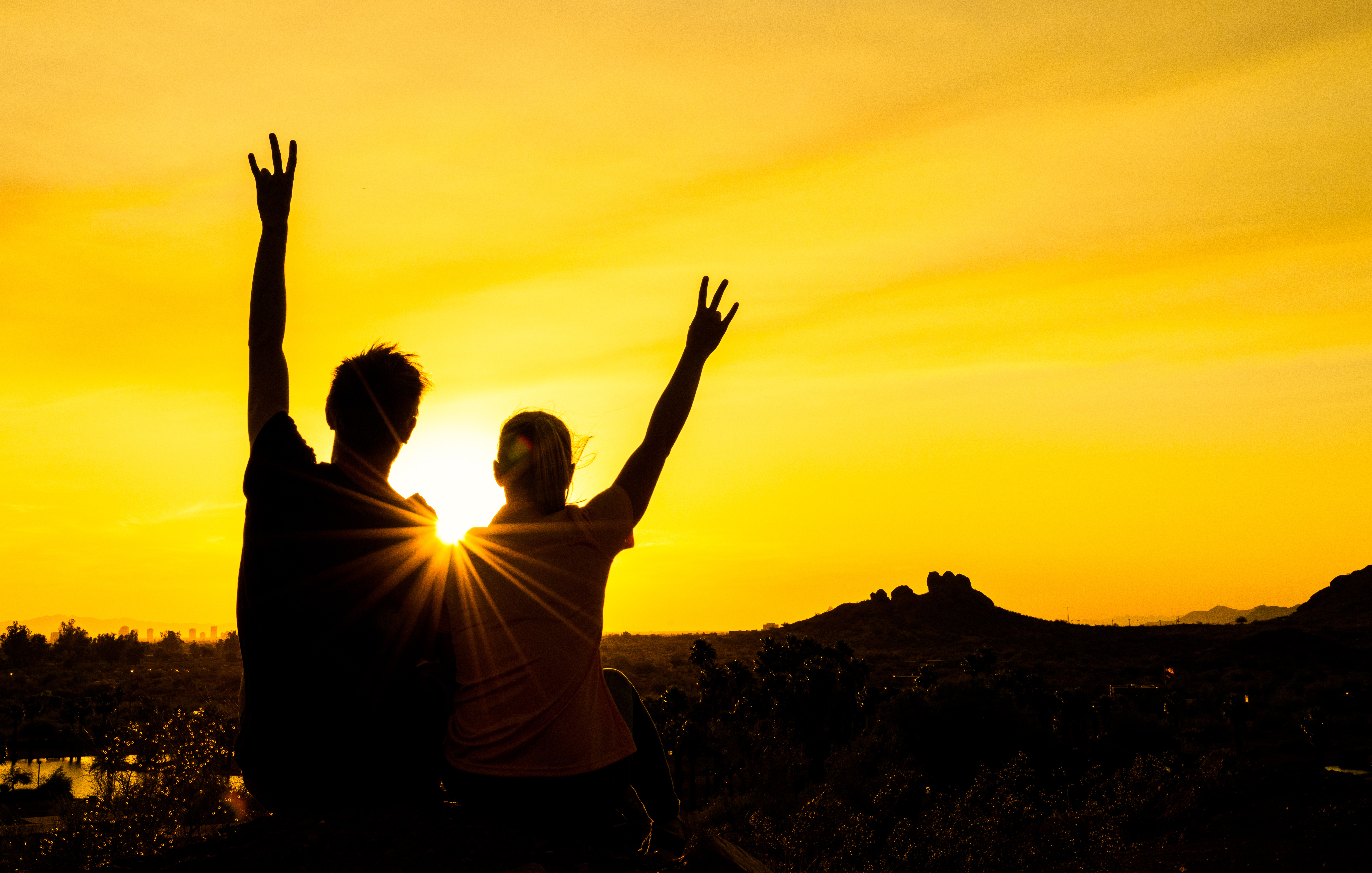 Two Sun Devils silhouetted by a golden sunset raise an arm in celebration.