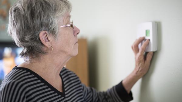 An elderly woman adjusting thermostat 