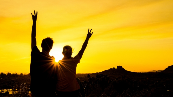 Two Sun Devils silhouetted by a golden sunset raise an arm in celebration.