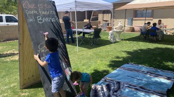 Children responding to prompt on chalkboard asking "What is your favorite part of your neighborhood?" in Spanish