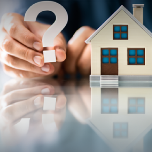 Hand holds a question mark sign next to a miniature model home